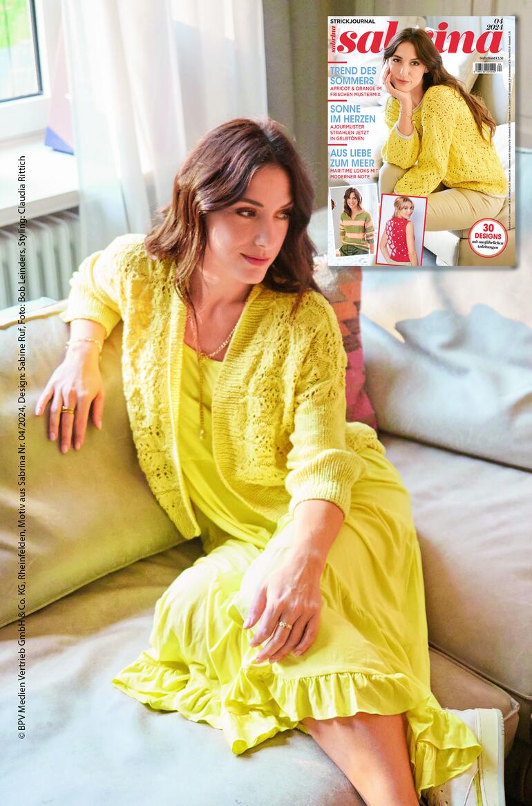 Frau in gelber Jacke sitzt auf einem Sofa, lächelt in die Kamera.