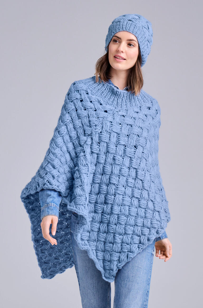 Frau in blauem Poncho und Mütze aus NewWool mit strukturiertem Muster.
