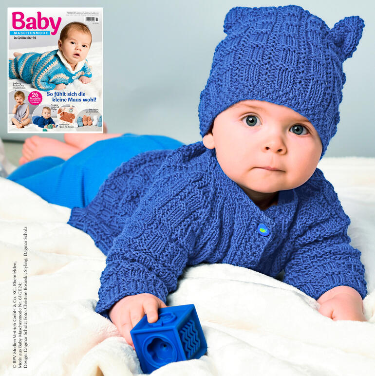 Babyjacke mit Mütze in blau aus Merino-Cotton, getragen von einem Baby in einem hellen Raum.