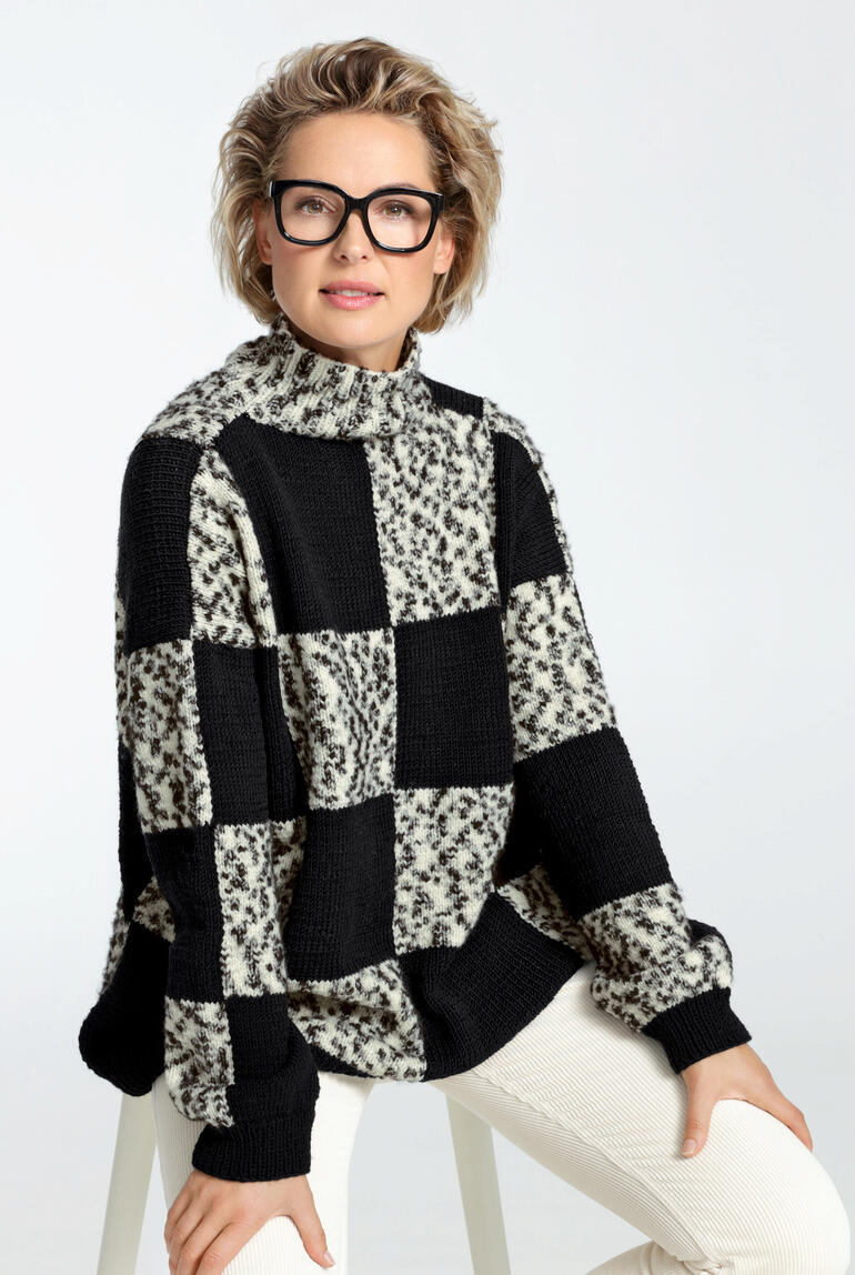 Frau mit Brille trägt einen karierten Pullover in Schwarz und Weiß, sitzt auf einem Hocker.