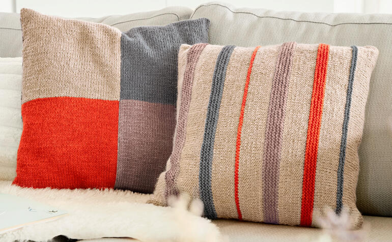 Zwei Kissenhüllen mit gestreiften Mustern auf einem hellen Sofa.