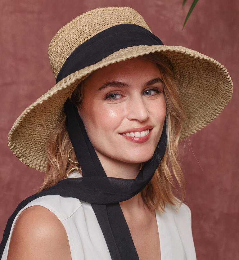 Nahaufnahme einer Frau im Eco Vita Raffia Hut mit schwarzem Band und lächelndem Ausdruck.