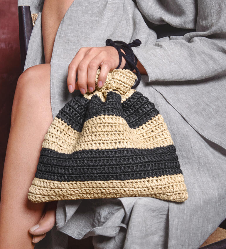 Gestreifte Tasche aus Eco Vita Raffia, gehalten von einer Frau in einem lässigen Outfit.