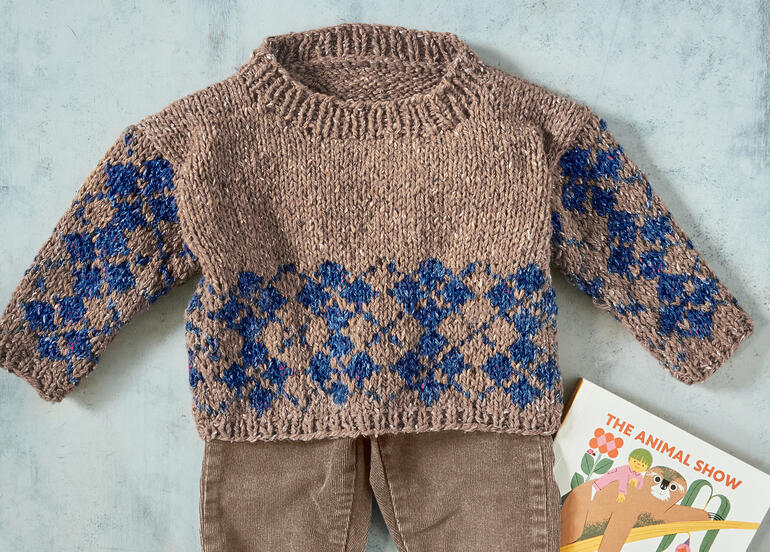 Baby-Pullover aus Punktino mit blauem Rauten-Muster und langen Ärmeln.