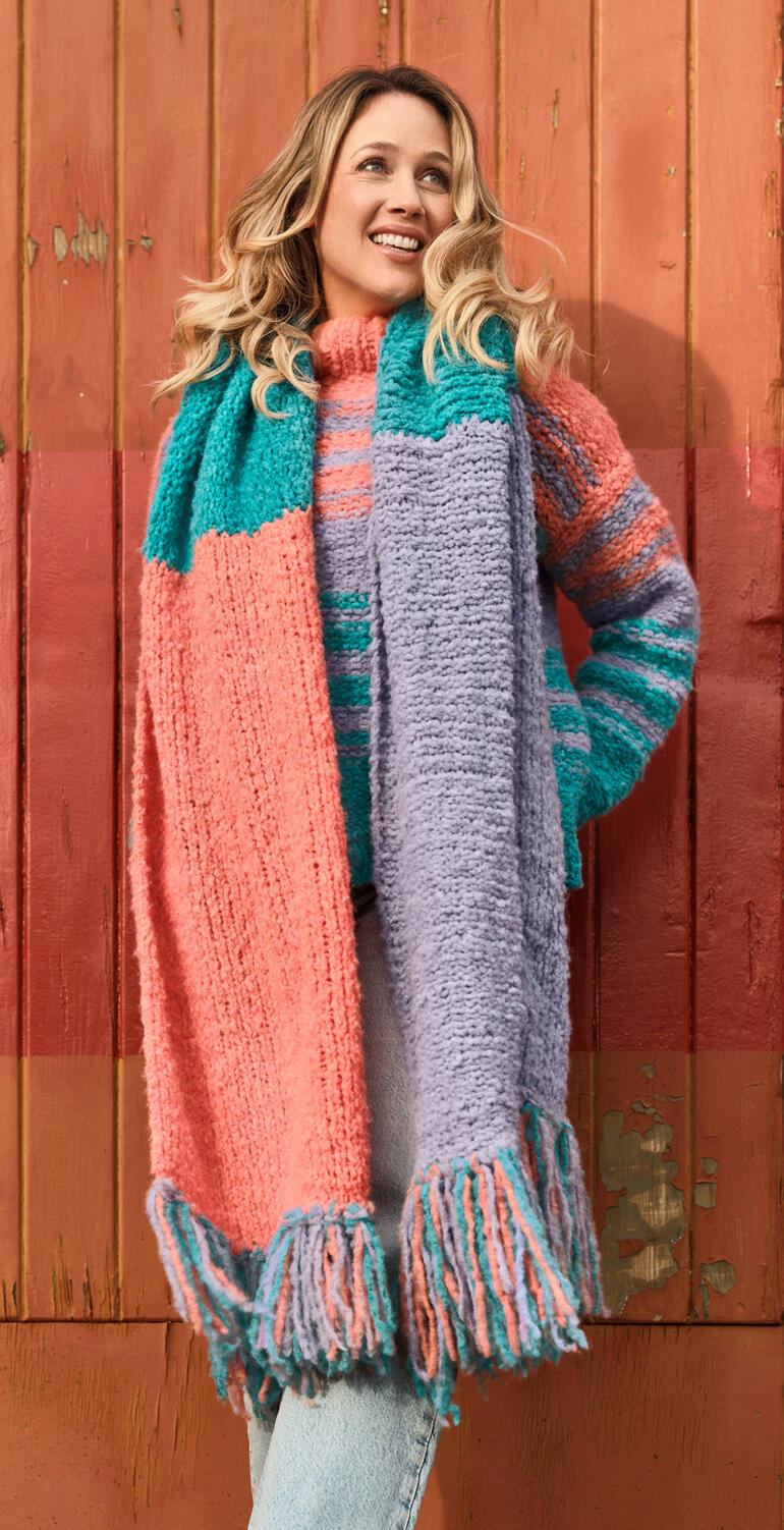 Frau in buntem Schal steht lächelnd an einer holzverkleideten Wand.