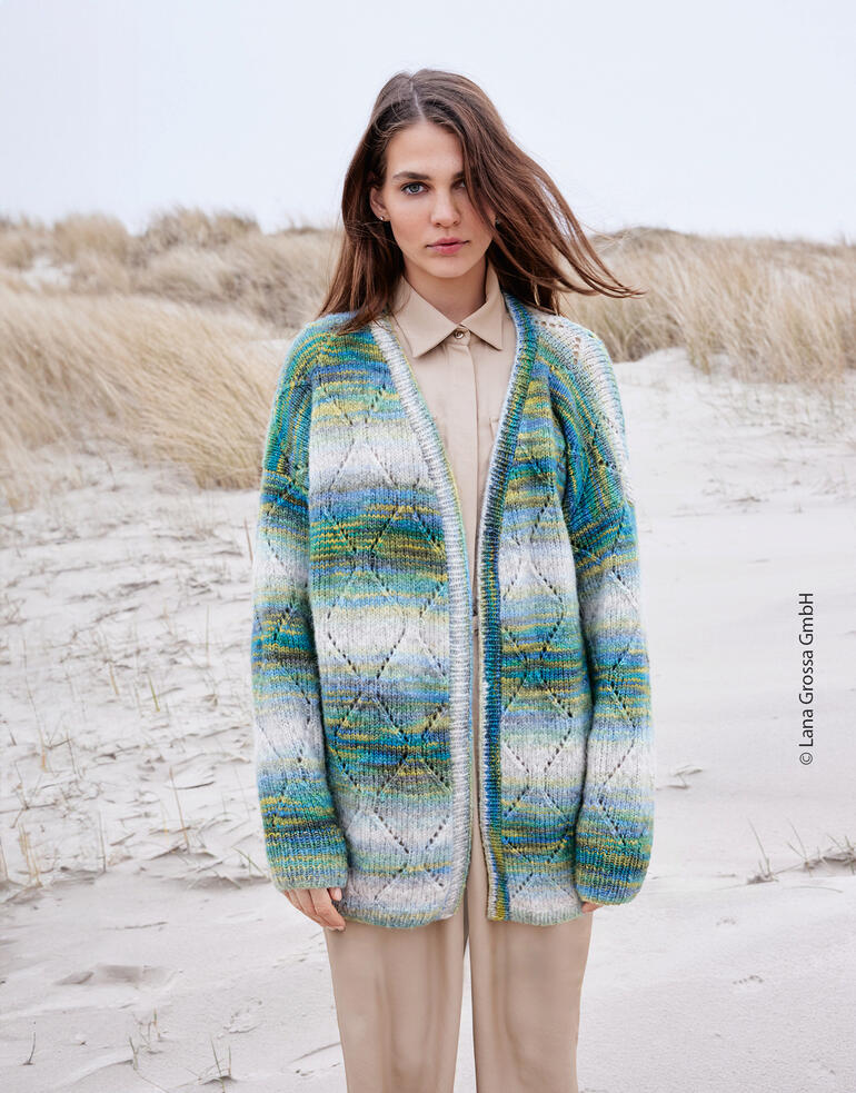 Bunte Cardigan aus Picasso-Garn, lässig über einem beigen Outfit getragen, am Strand.