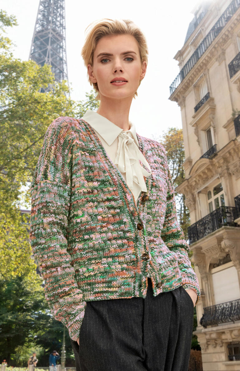 Bunte Jacke aus Merino-Print, elegant über einem dunklen Outfit im Freien getragen.