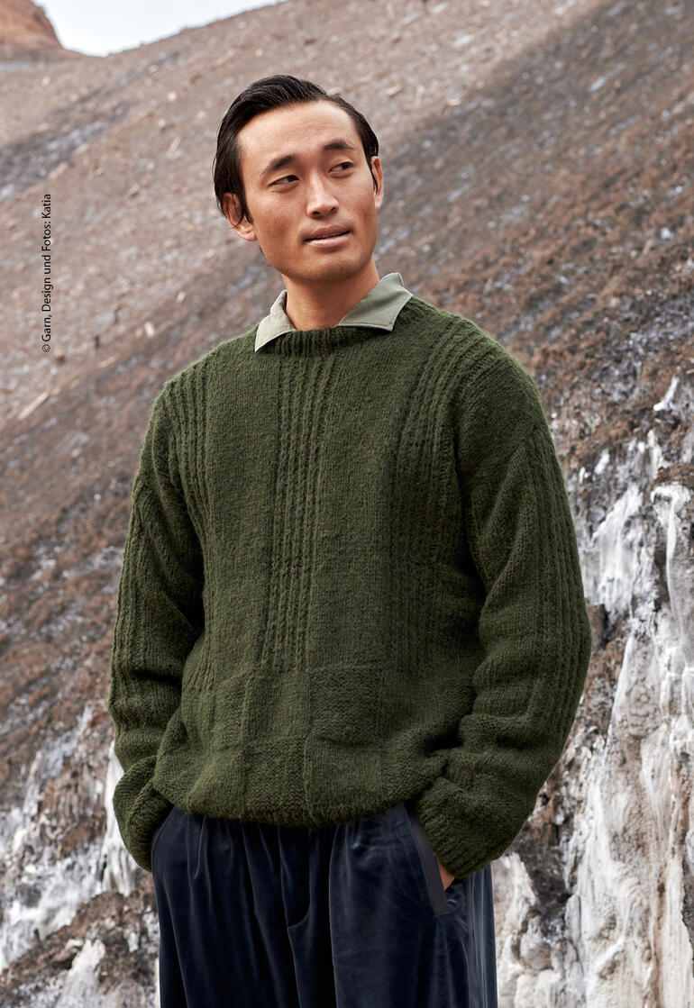 Mann in grünem Pullover mit strukturiertem Muster, der lässig im Freien steht.