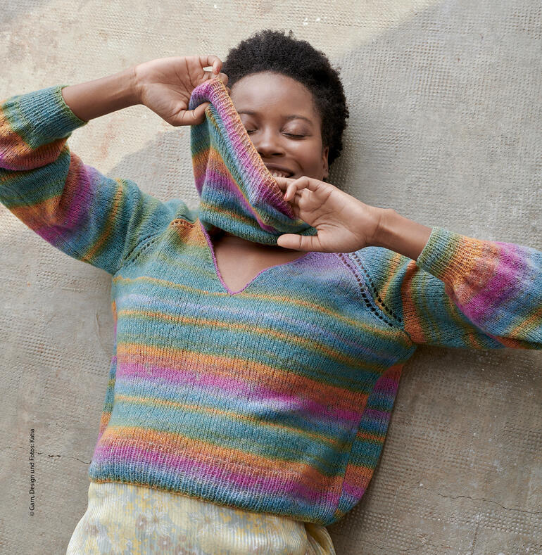 Lächelnde Frau in mehrfarbigem Pullover mit V-Ausschnitt, die den Pullover anhebt.