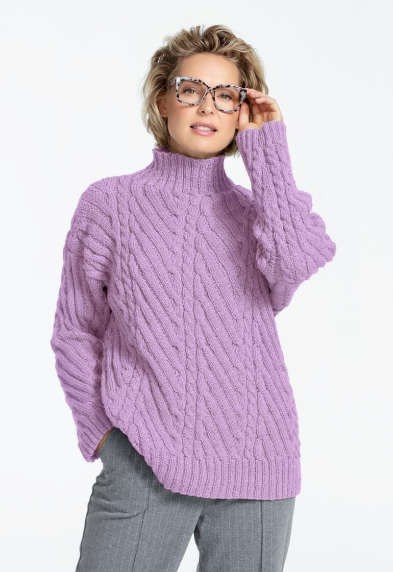 Frau in rosa Pullover mit Zopfstruktur und Brille, die die Hand an den Kopf legt.