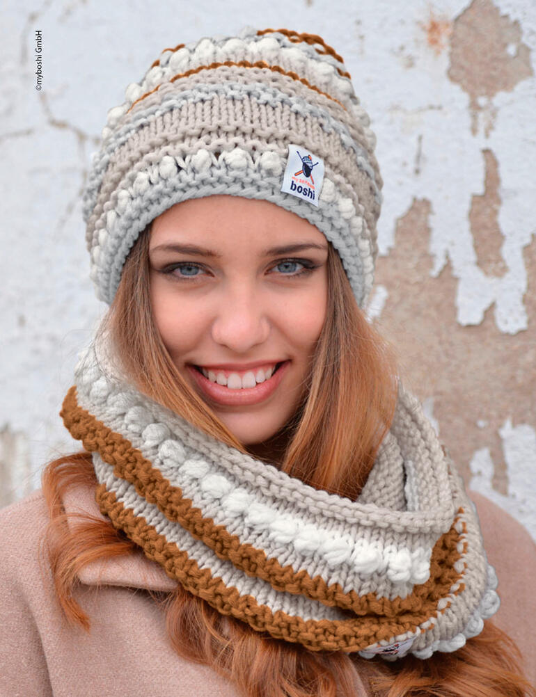 Junge Frau trägt eine graue Mütze mit Loop und lächelt in die Kamera.