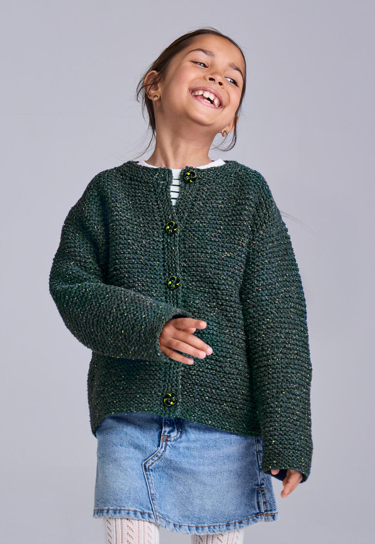 Lachendes Mädchen trägt eine grüne Kinderjacke aus Punktino mit lila Knöpfen.