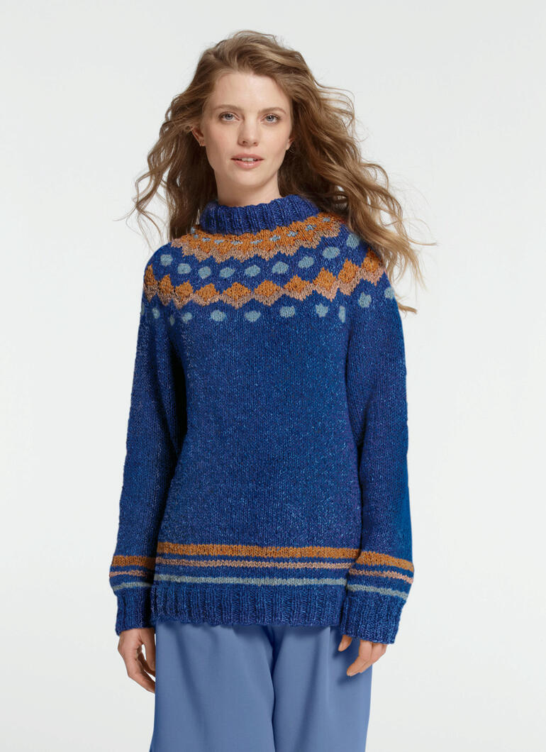 Junge Frau in einem blauen Pullover mit buntem Muster und Rollkragen in lässiger Pose.