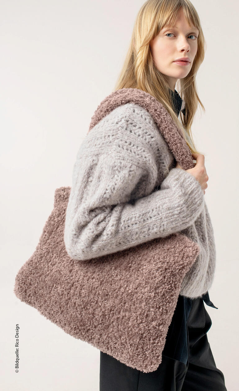 Frau trägt eine große Tasche aus flauschigem Material in beige und posiert lässig.