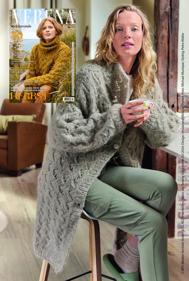 Frau im grauen, langen Nappymantel mit großen Knöpfen in einem gemütlichen Raum.