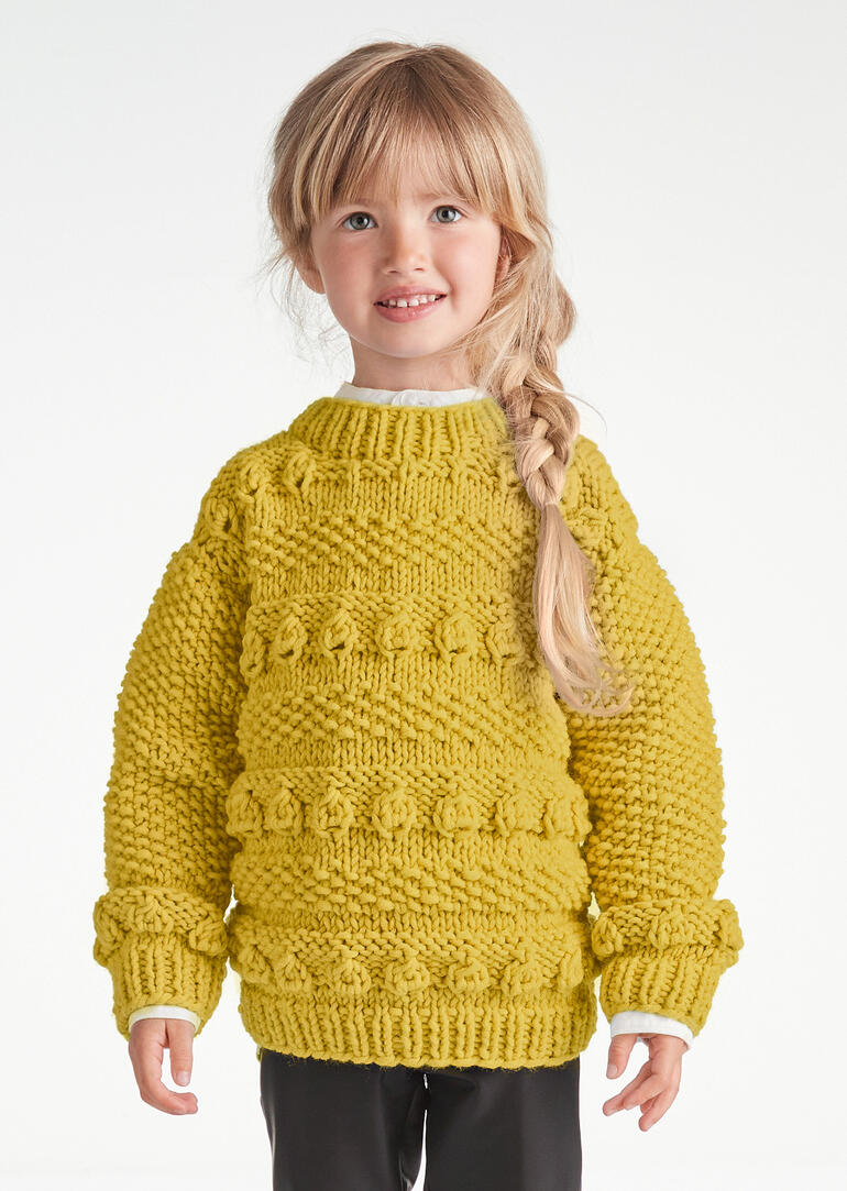 Kleines Mädchen trägt leuchtend gelben Pullover aus Merino Dick, lächelt.
