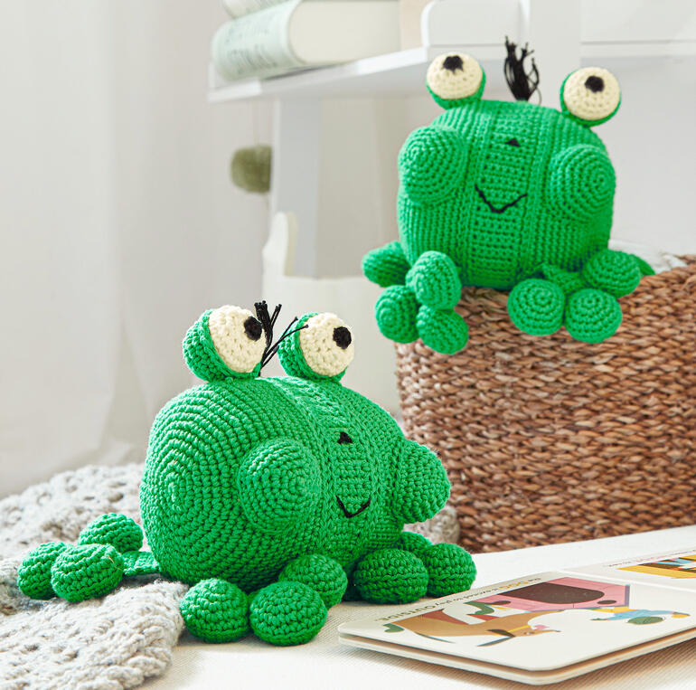 Zwei gehäkelte Frosch-Spielzeuge auf einem Tisch, spielen zusammen.