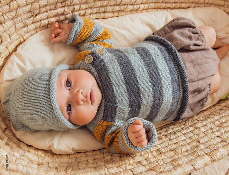 Baby im gestreiften Babypullover aus Baby Dream dk Uni, liegt entspannt in einer Korbliege.