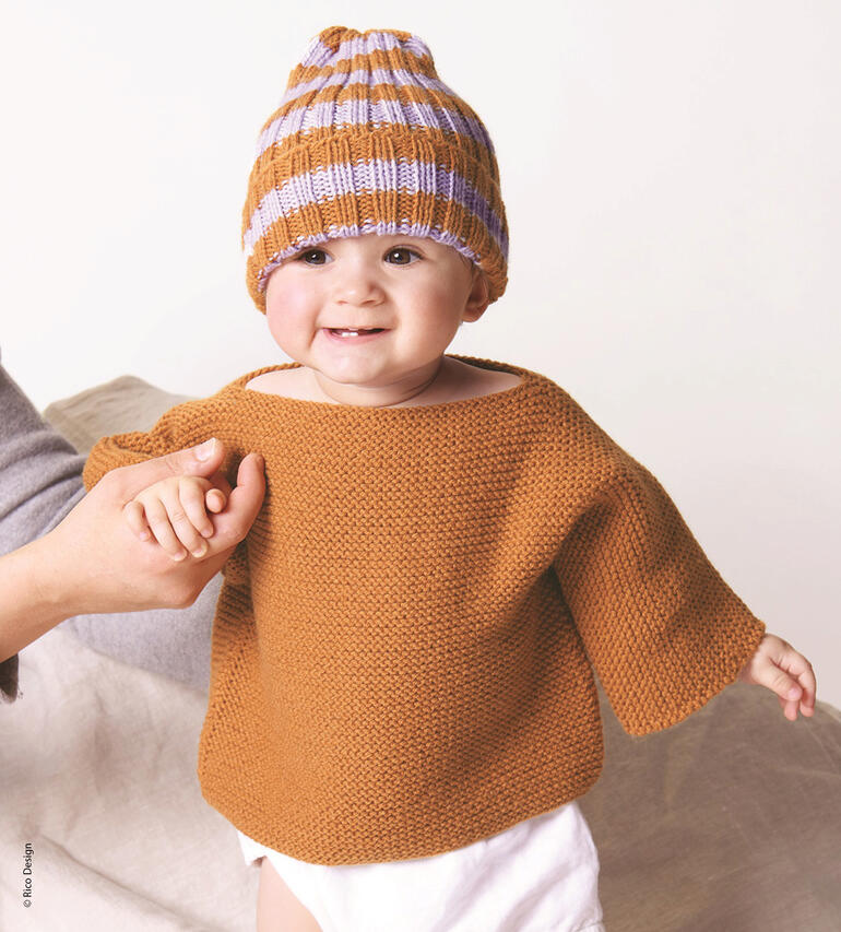 Lachendes Baby in braunem Pullover und Mütze, gehalten von einer Person.