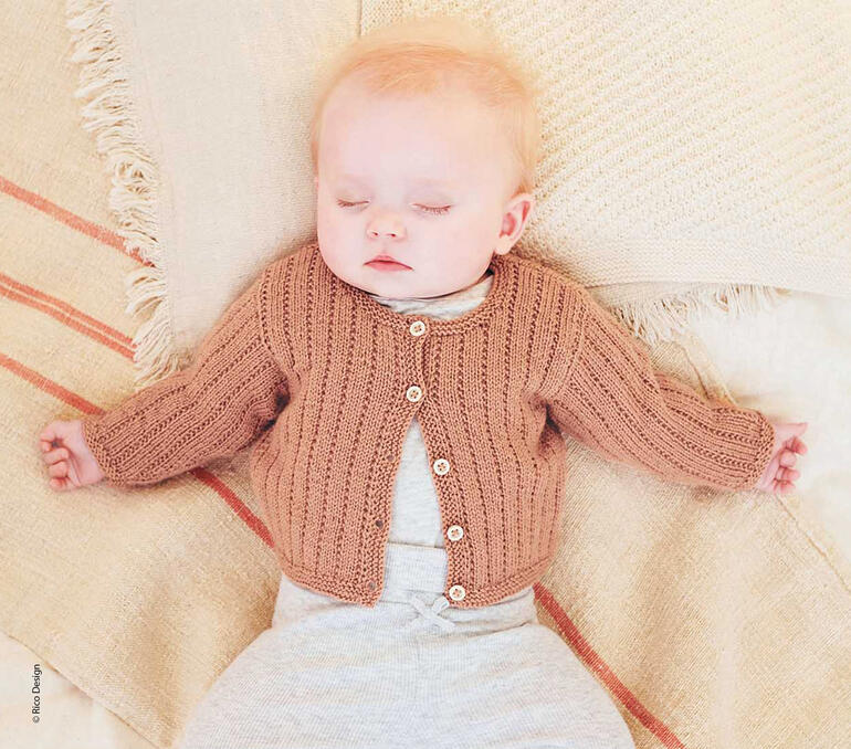 Schlafendes Baby in beiger Strickjacke auf einer Decke.