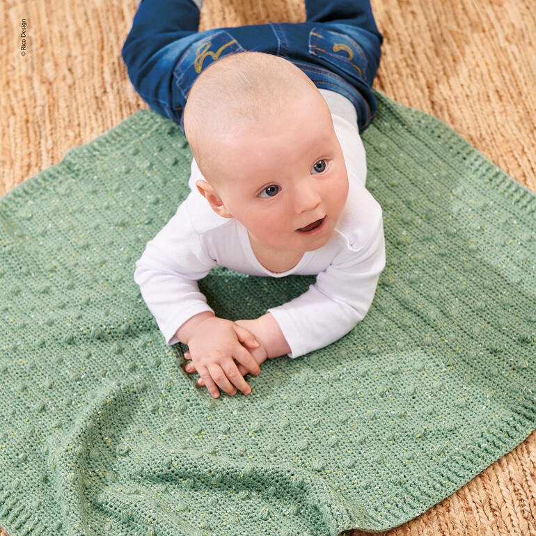Baby krabbelt auf einer grünen Häkeldecke.