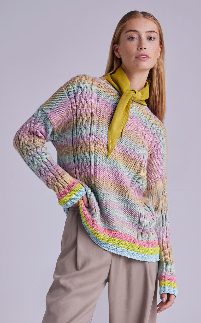 Frau in buntem Pullover mit Halstuch, vor neutralem Hintergrund.