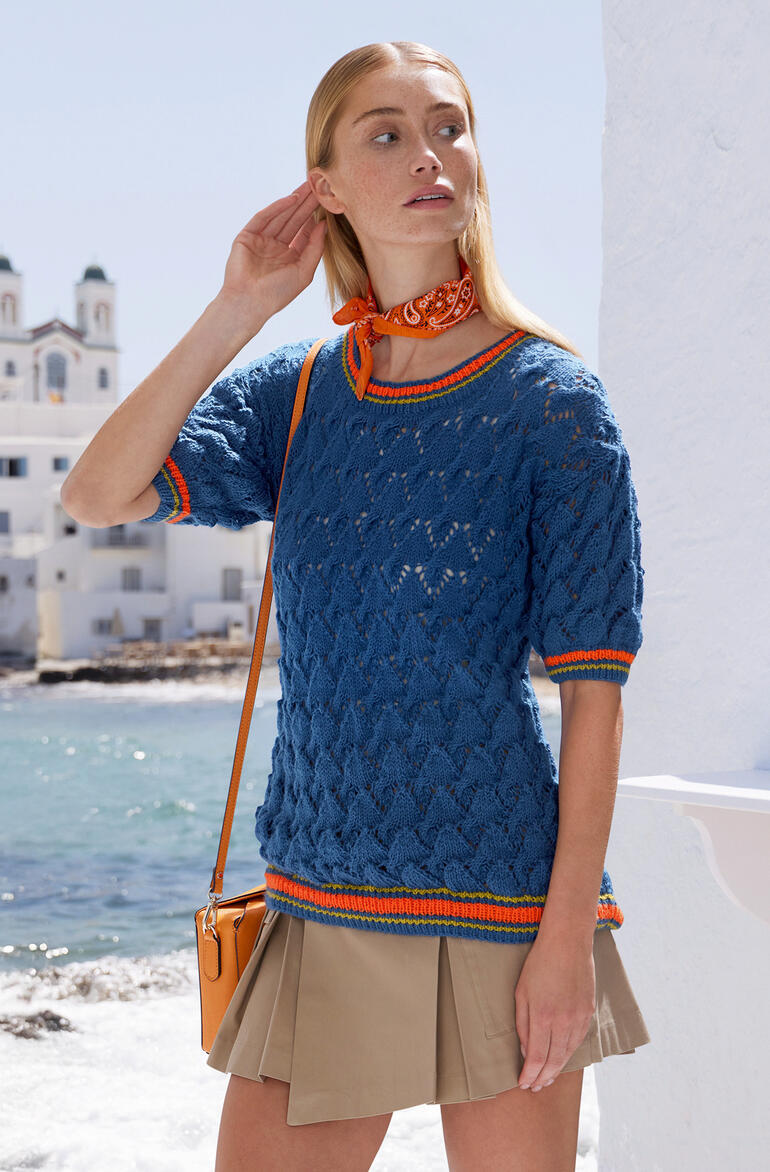 Türkiser Kurzarm-Pulli mit modernem Muster, getragen von einer Frau in einem maritimen Setting.