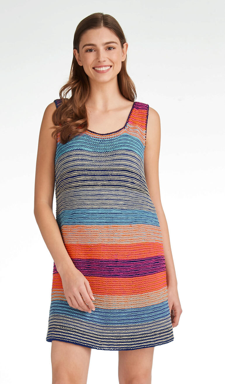 Frau in buntem, gestreiftem Long-Top steht lächelnd vor einem hellen Hintergrund.