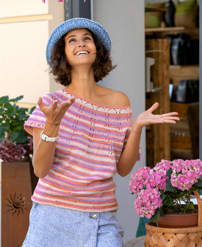 Frau in gestreiftem Top und blauen Jeans lächelt vor blühenden Pflanzen.
