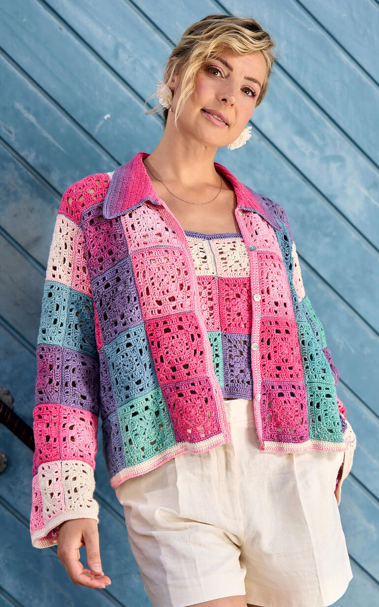 Frau in farbenfroher Häkeltasche über einem Häkeltop, posiert vor einer blauen Wand.