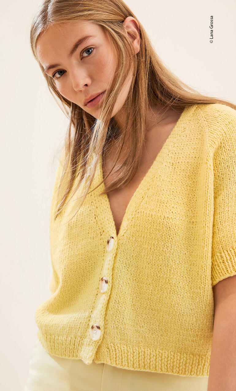 Frau in gelber Raglanjacke mit tiefem V-Ausschnitt, posiert freundlich.