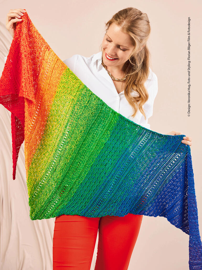 Frau hält ein farbenfrohes, quer gehäkeltes Tuch, lächelnd und freudig.