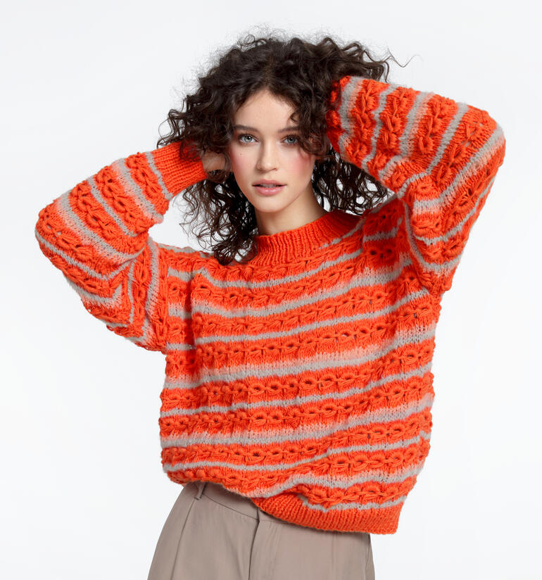 Frau trägt einen orangen Pullover aus Babyboomer und Aerea, lächelnd