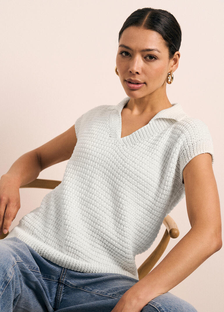 Frau in hellgrünem Poloshirt mit Struktur, sitzt entspannt in einem Holzstuhl.