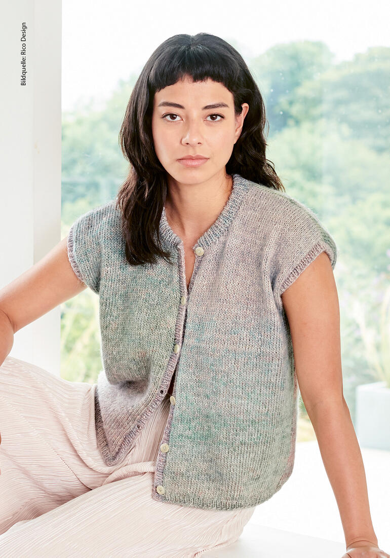 Frau in einer Weste aus Creative Painted Power Cotton dk von Rico Design, sitzt in einem hellen Raum.