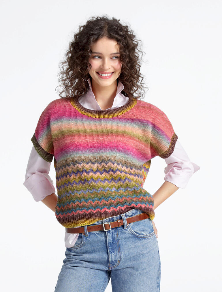 Frau in einem bunten Pullunder aus Pinterella von Junghans-Wolle, trägt Jeans und lächelt.