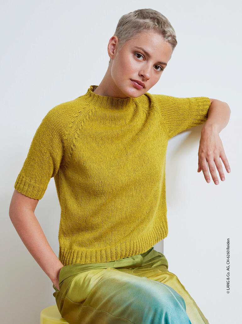 Frau in einem kürzeren Pullover aus Ananas von LANG Yarns, sitzt entspannt mit einem farbenfrohen Rock.