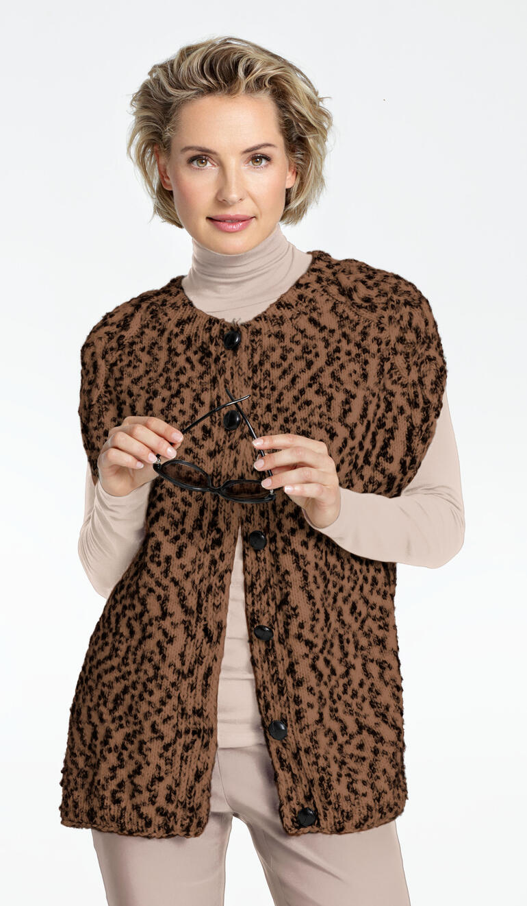 Frau in brauner, pelzartiger Oversize-Weste über einem beigen Oberteil.