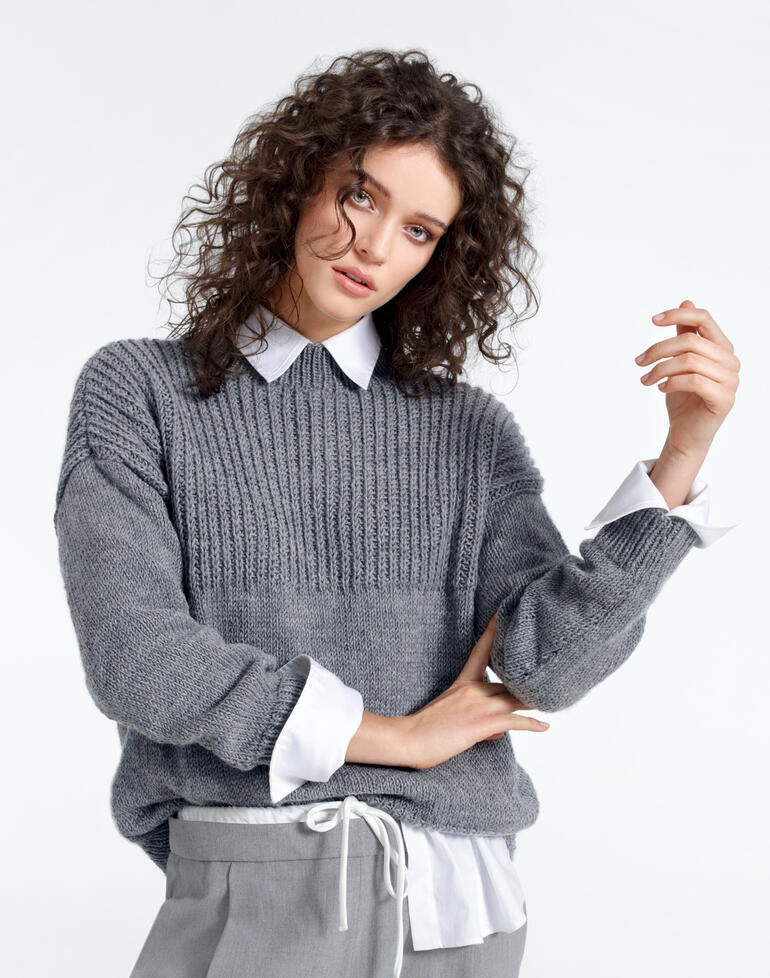 Frau in einem grauen Pullover aus Merino-Extrafein, leicht lächelnd