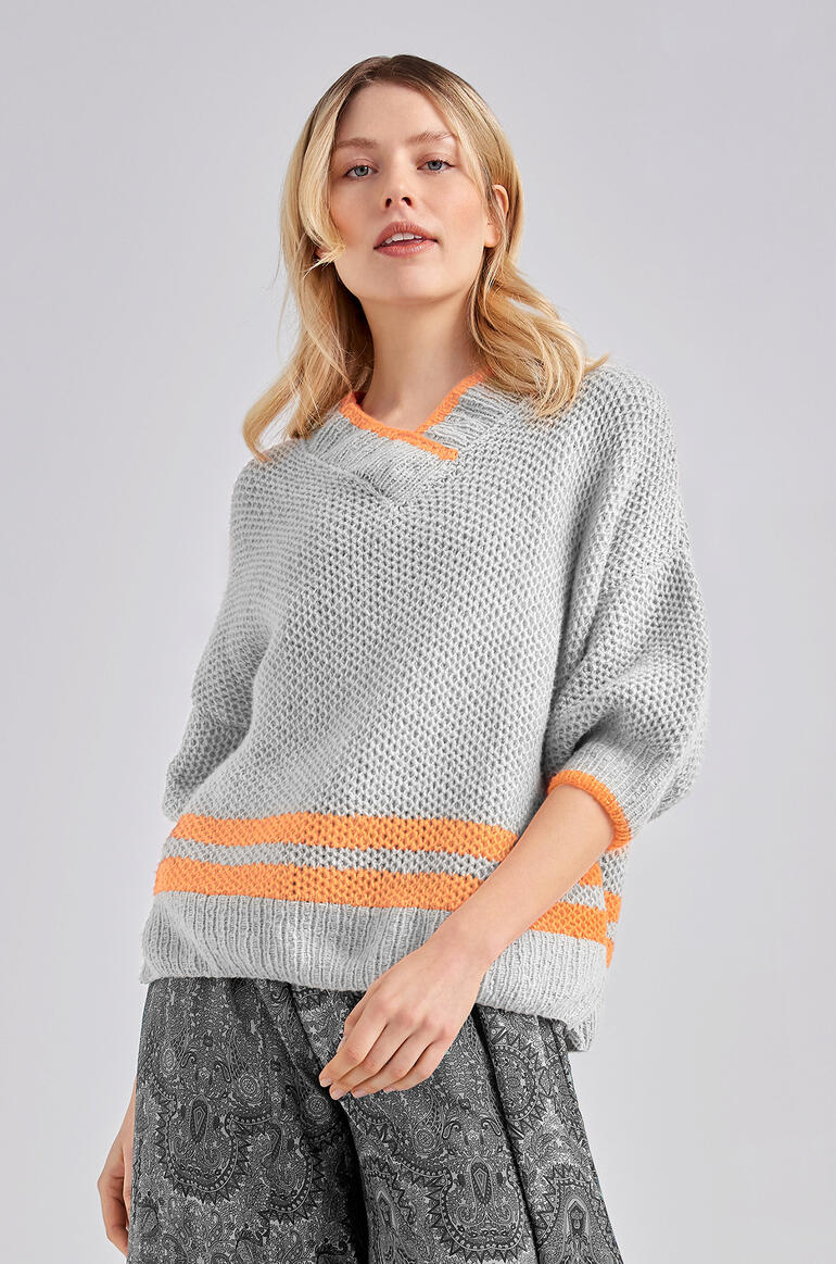 Frau trägt einen grauen Pullover aus Charme mit orangefarbenen Streifen.