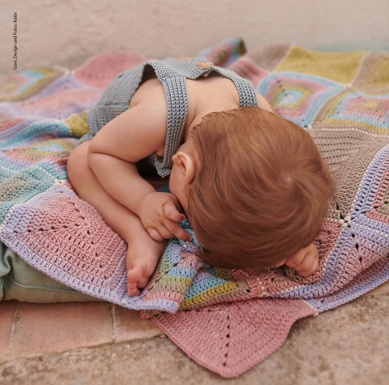 Schlafendes Kind liegt auf einer bunten Decke und greift danach.