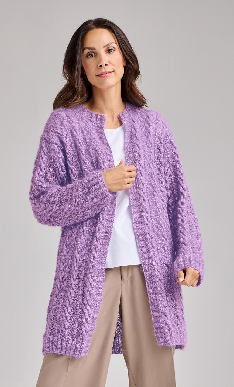 Frau in einer langen, offenen lila Jacke aus dickem Strick, trägt ein einfaches Unterhemd.