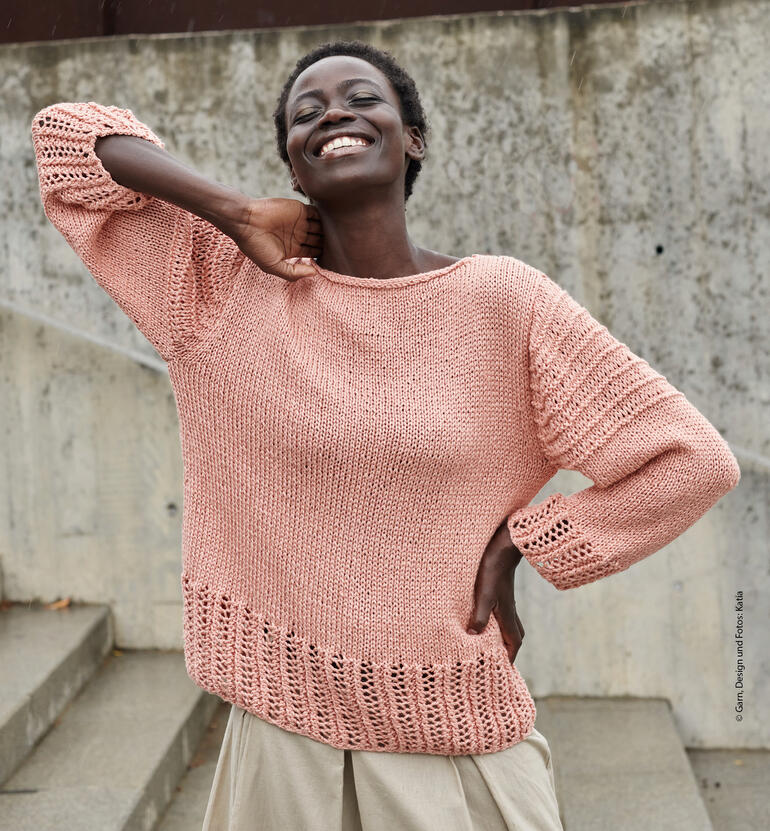 Frau in rosafarbenem Pullover mit lässigem Look, lächelt in urbaner Umgebung