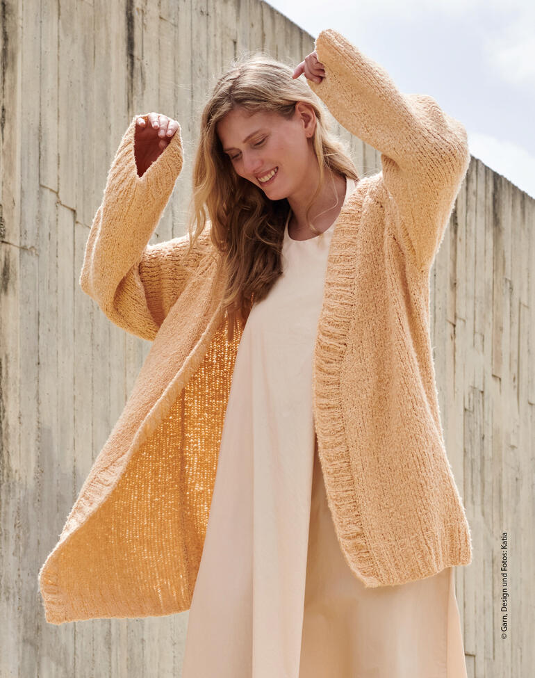 Frau in beigefarbener Jacke, die geöffnet getragen wird, lächelt vor trockener Wand