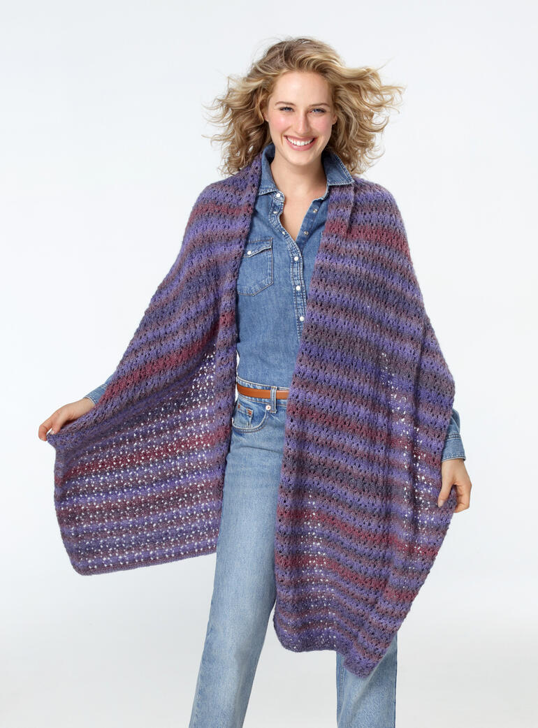 Frau präsentiert ein gemustertes Tuch aus Batique bei Tageslicht, im Freien.