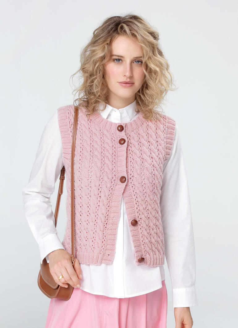 Frau in zart rosa Weste mit Knöpfen, kombiniert mit einer langen blauen Jeans.