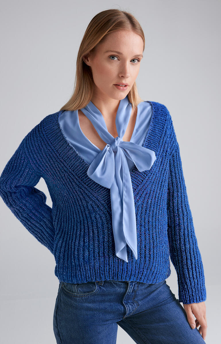 Blauer Pullover aus Punktino, weibliches Model mit Schleife am Hals.