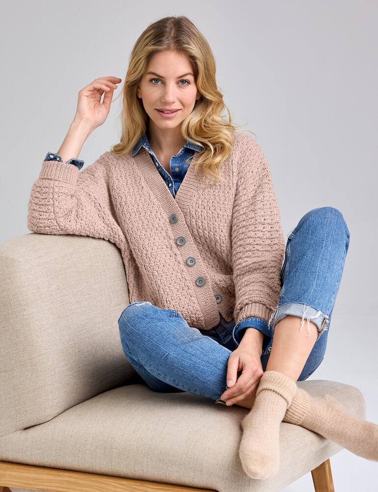 Beige Jacke aus Enny, weibliches Model sitzt bequem auf einem Sofa.