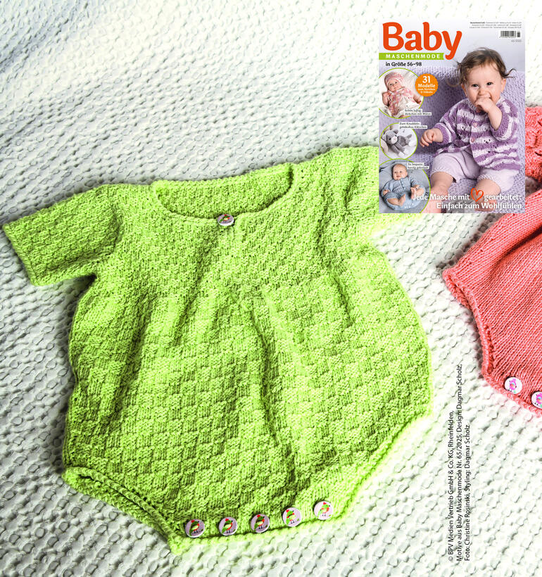 Grüner Babybody auf einer weißen Decke, umgeben von zwei weiteren Bodys.