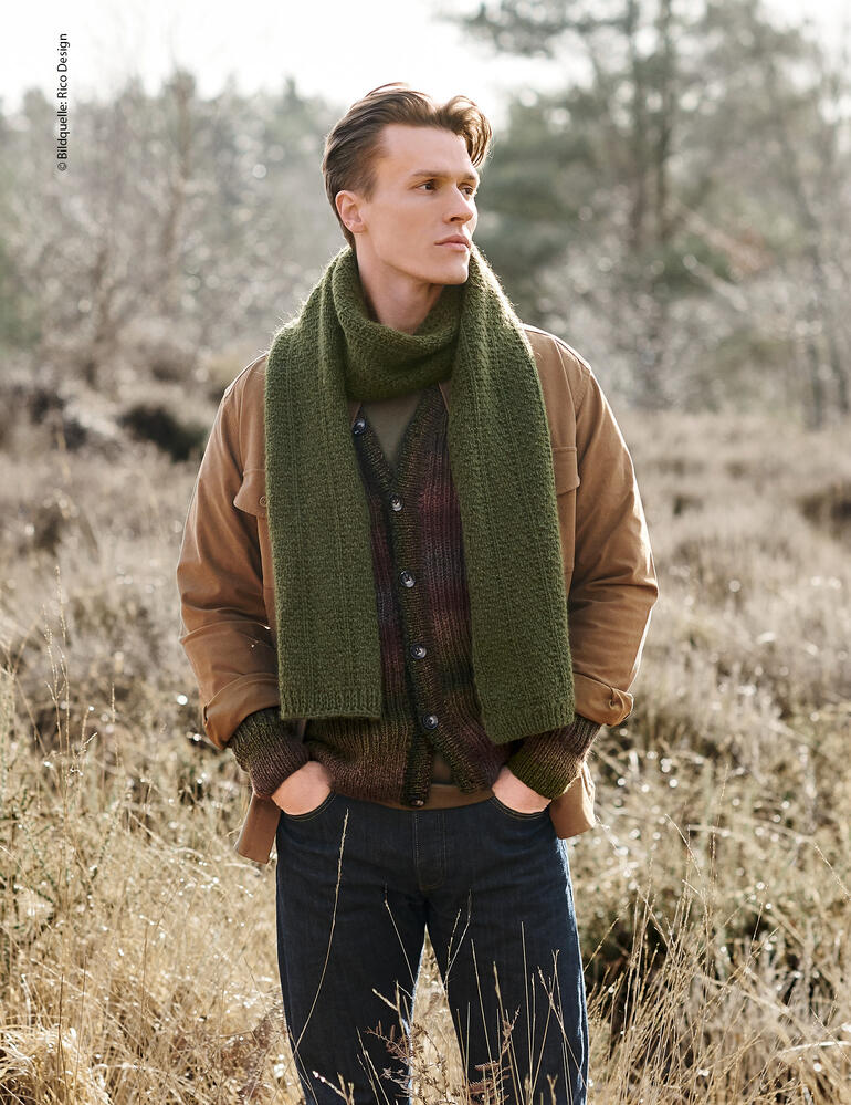 Mann in grünem Schal steht im Wald, lächelt in die Kamera.